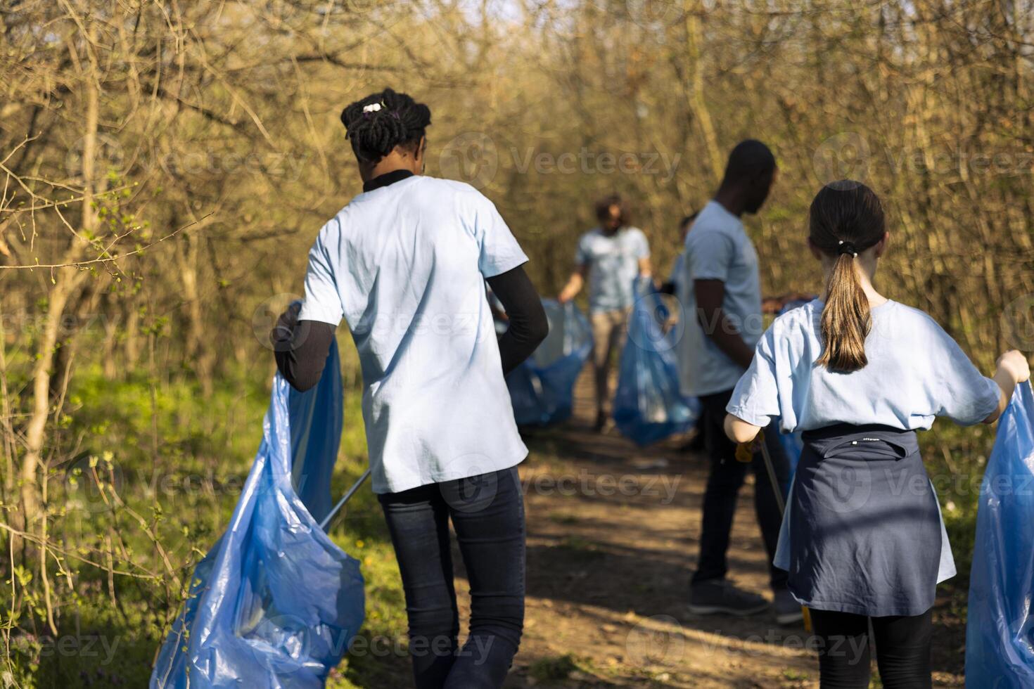 African american girl working with a team of ecologists to collect junk and plastic from the natural environment. Recycling in a bag, doing voluntary work to protect the ecosystem. photo