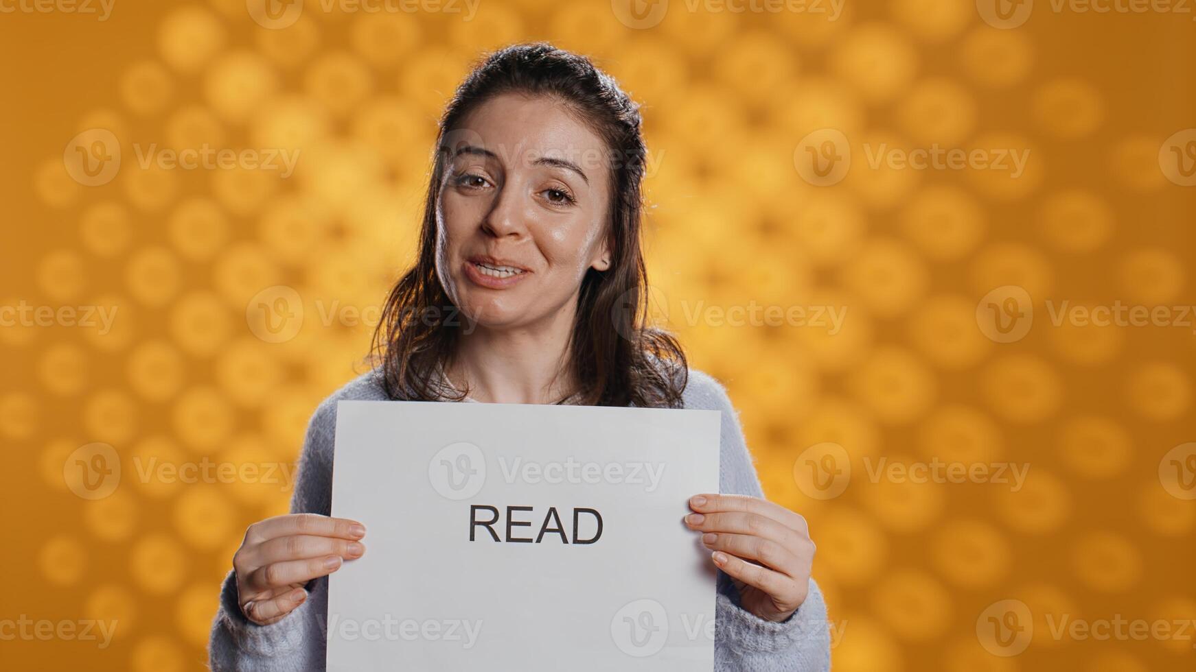 Woman holding message in hands urging people to read more, talking about importance of lecture, isolated over studio background. Bookworm promoting literacy concept, camera B photo