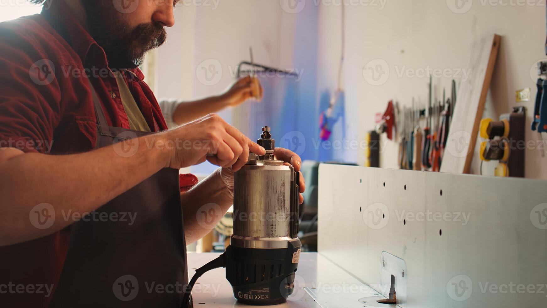 Serviceman in furniture assembling shop changing rotor part on spindle moulder machinery. Engineer in woodworking studio fixing defective wood shaper, replacing damaged component, camera B photo