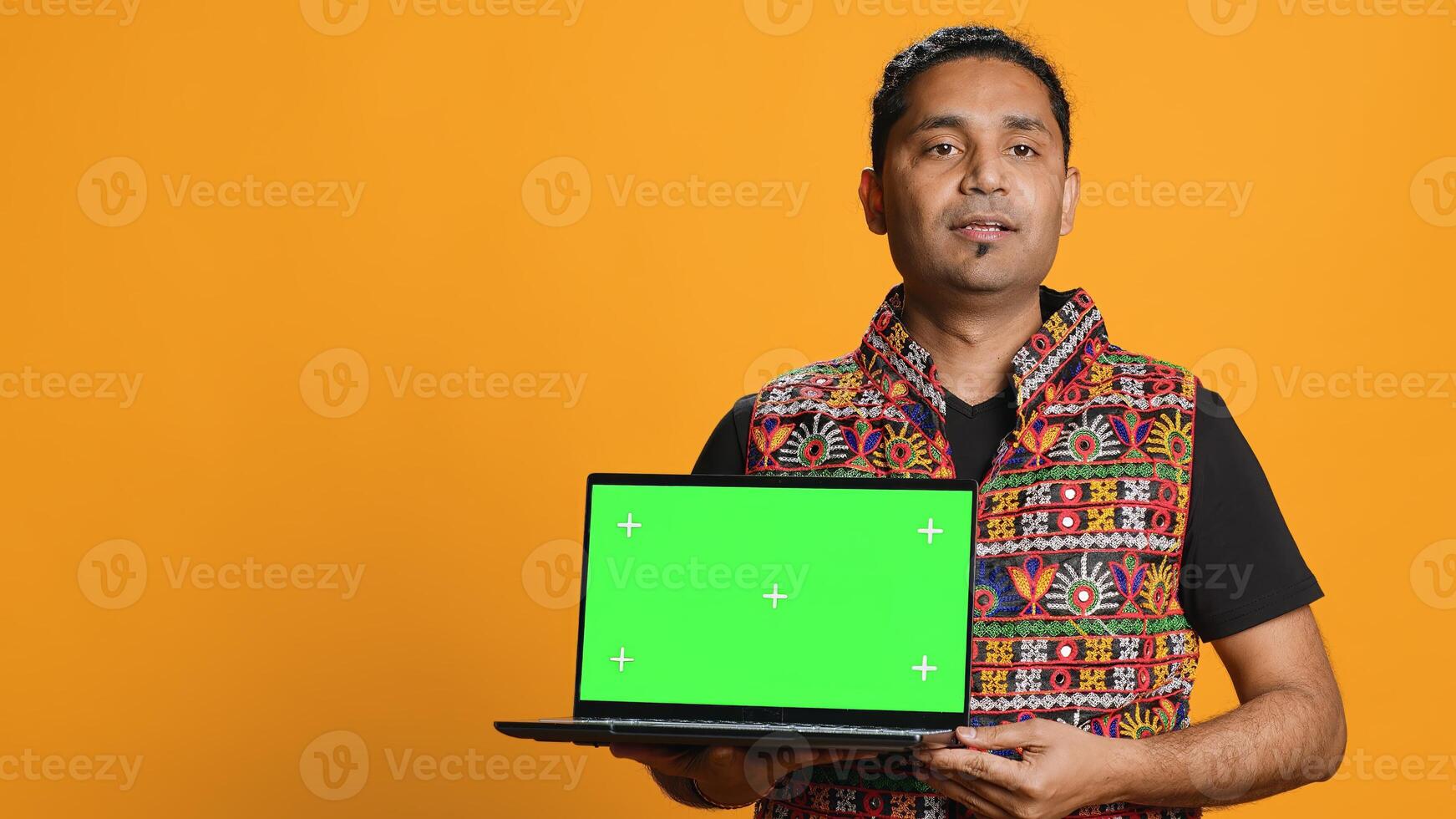 Upbeat tech specialist doing promotion using isolated screen laptop, studio background. Cheerful indian person holding chroma key notebook, doing advertisement for it, camera A photo