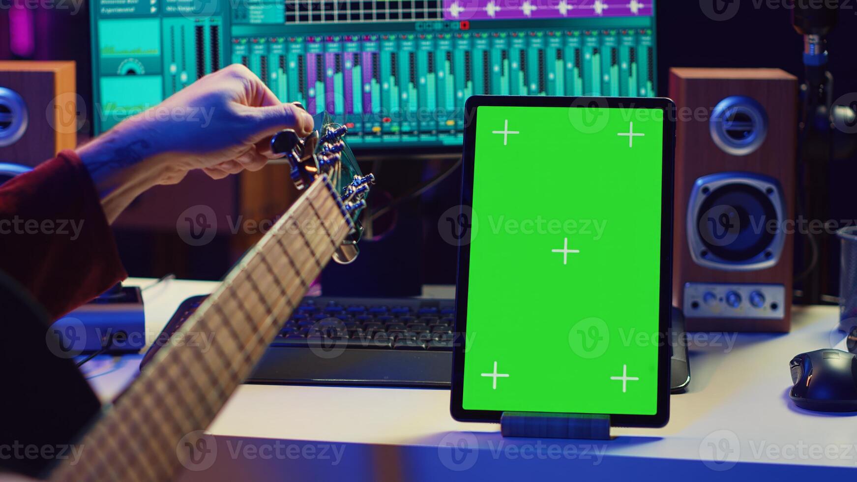 Audio engineer practices tuning his acoustic guitar in home studio, watching a tutorial online via tablet with greenscreen. Musician learning to play instrument and create music. Camera A. photo