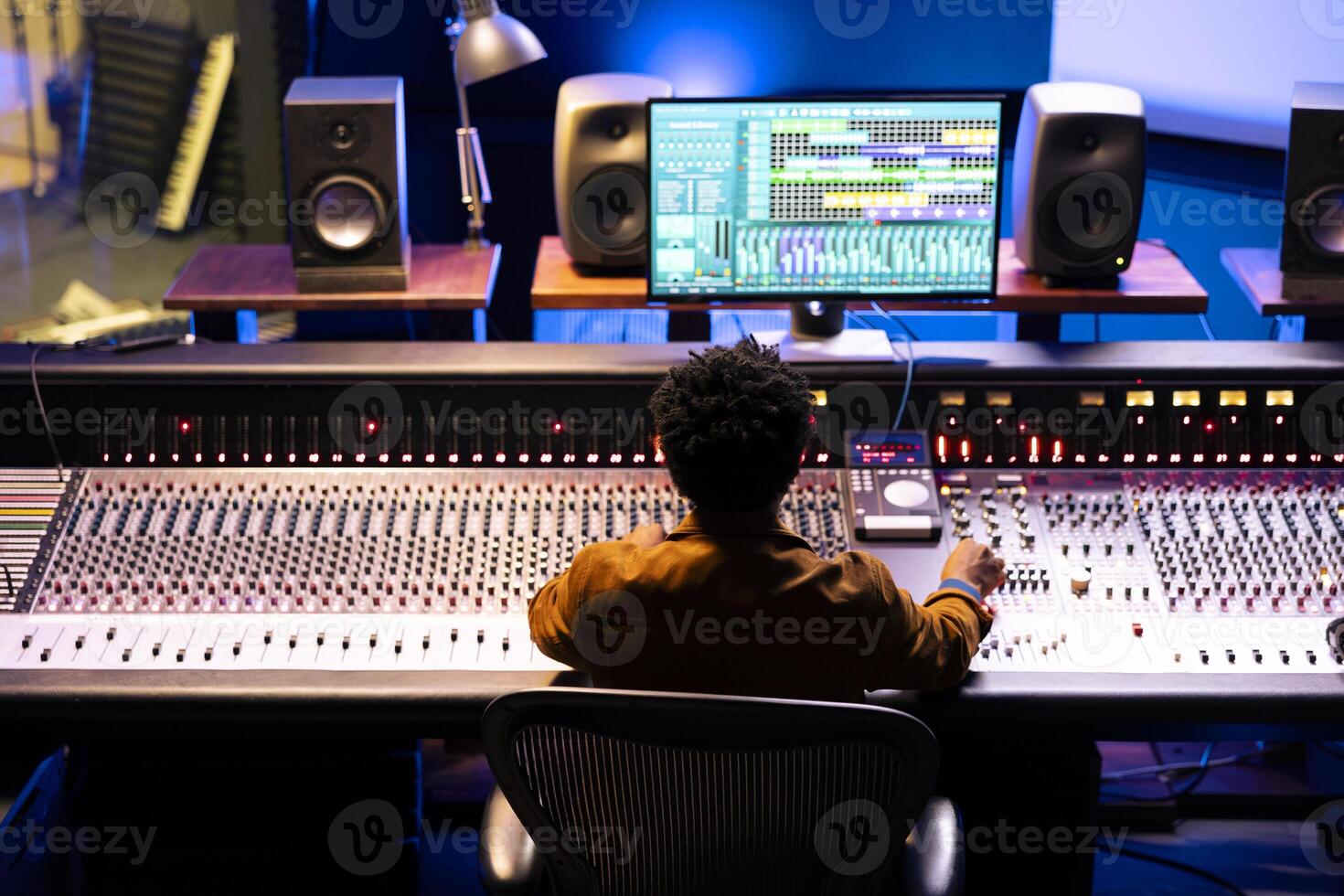 Joyful sound designer finishing a new hit song in music recording studio, working with digital audio software and console in control room. Technician producing records with soundboard panel. photo