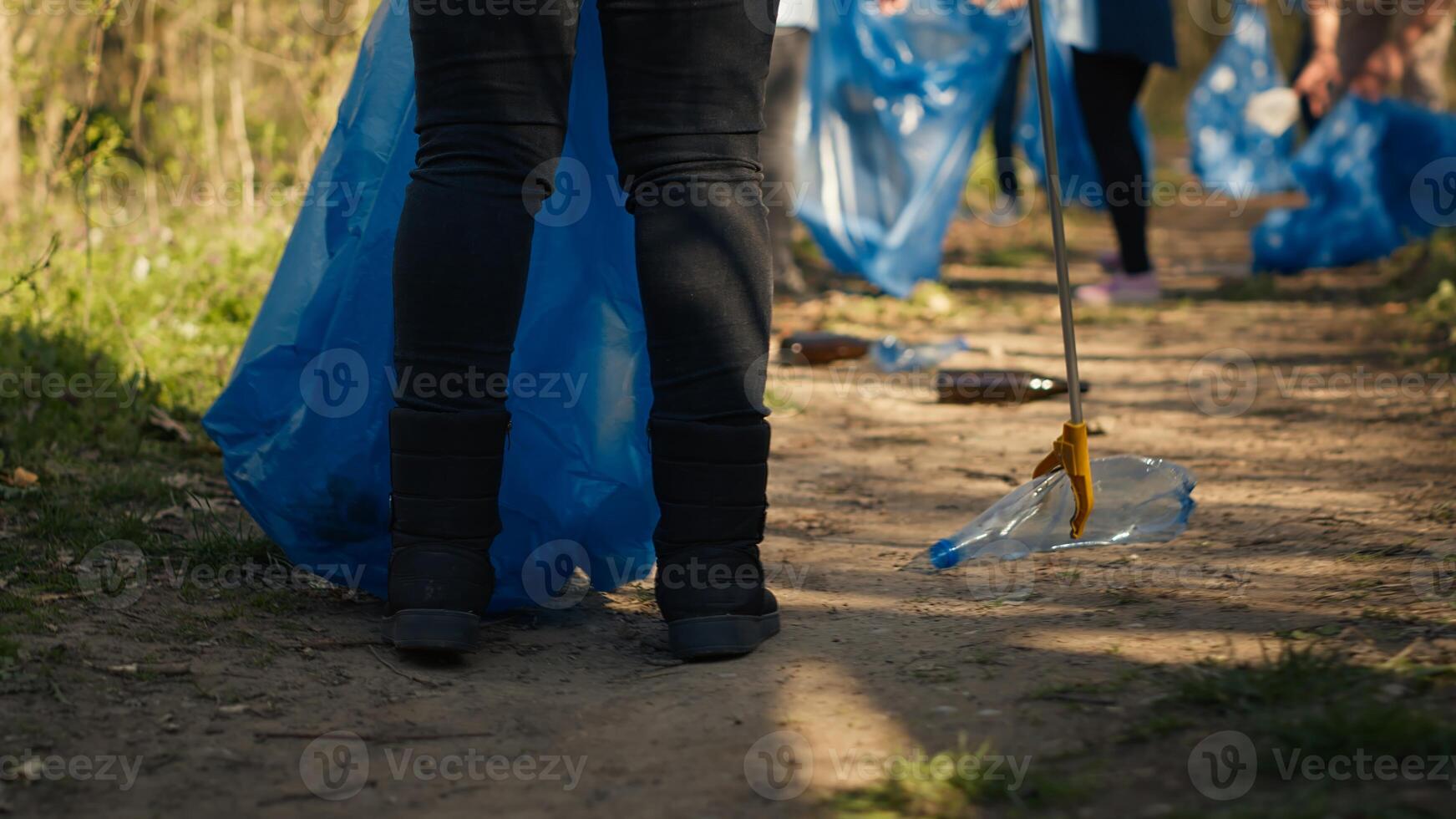 Diverse activists group using claw tools to grab trash and plastic, storing it in garbage disposal bags. People gathering to collect rubbish and recycling for sustainable lifestyle. Camera A. photo