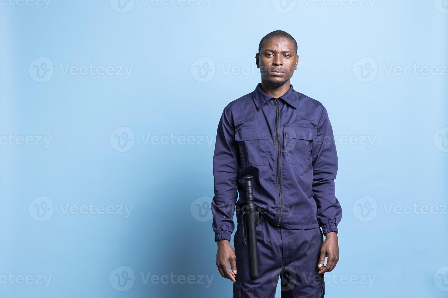Portrait of african american security officer posing in studio, wearing a patrolling service uniform equipped with a baton for his own protection. Guard on duty shows his authority. photo