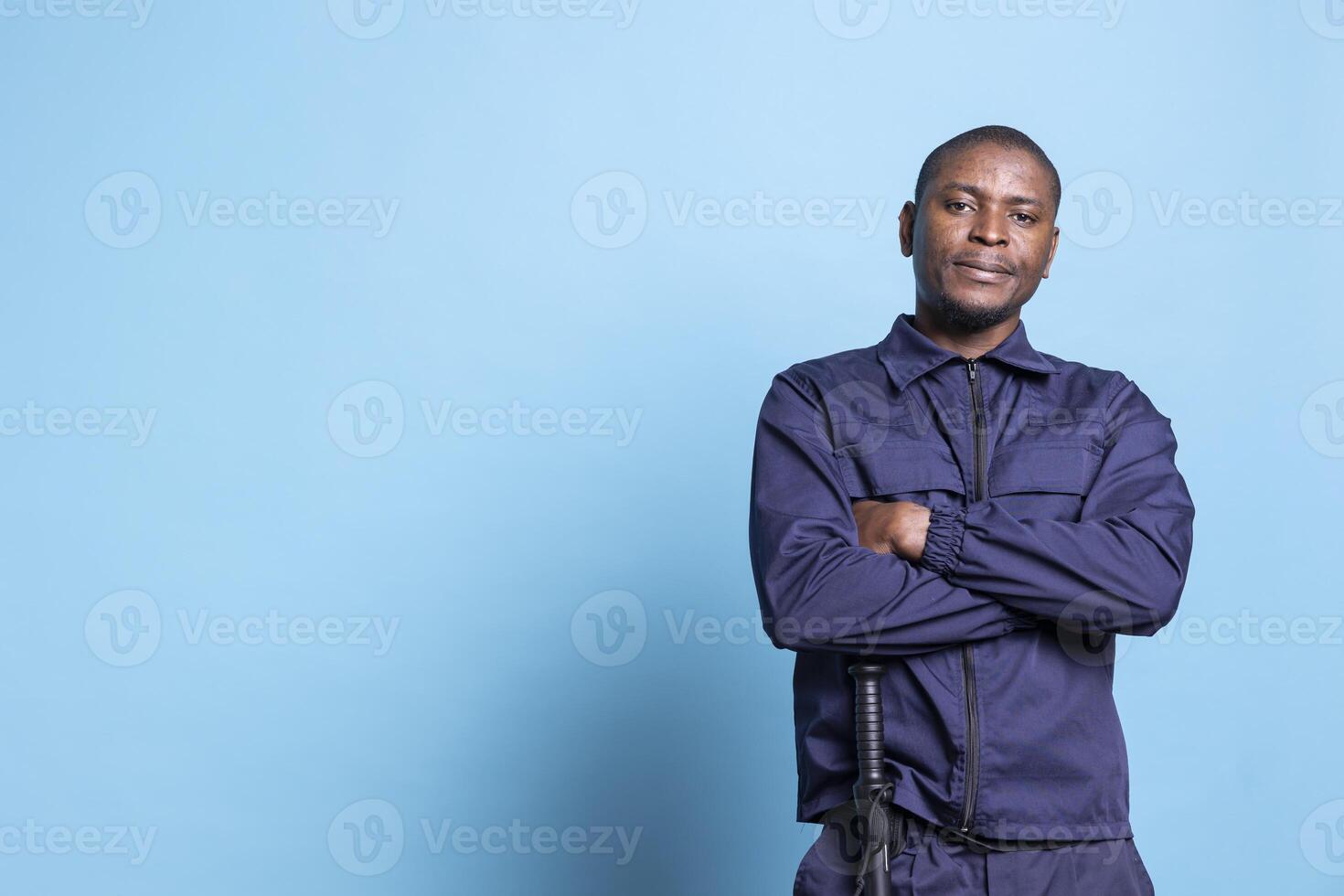 Portrait of proud security officer posing with arms crossed on camera, wearing his patrolling uniform with confidence and devotion. Trained armed bodyguard works on protection and safety. photo
