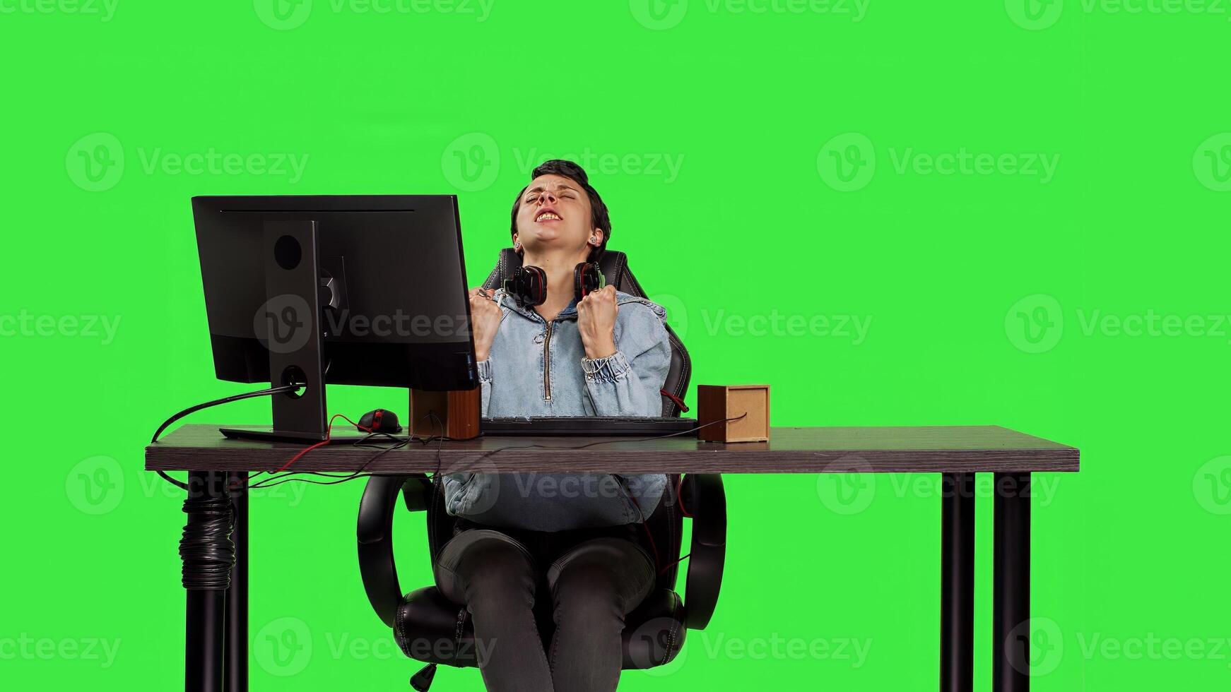 Young woman playing games online on pc at desk against greenscreen backdrop, winning global e sport championship on computer. Player feeling joyful and content with her victory. Camera B. photo