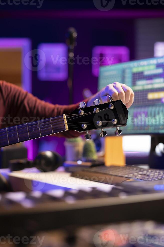 Producer tuning his acoustic instrument to record new sounds, working in his home studio to create new cool music. Musician performer playing guitar with mixing and mastering tools. Close up. photo