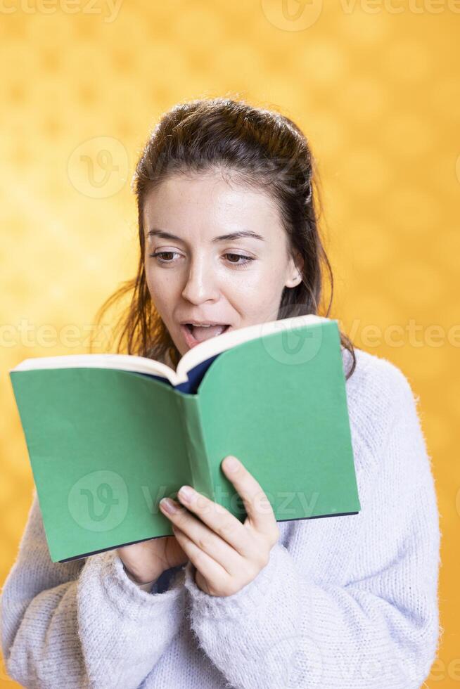 Woman gasping while reading intriguing book, feeling surprised, enjoying hobby during leisure time. Amazed person astounded by novel story plot twists, isolated over studio background photo