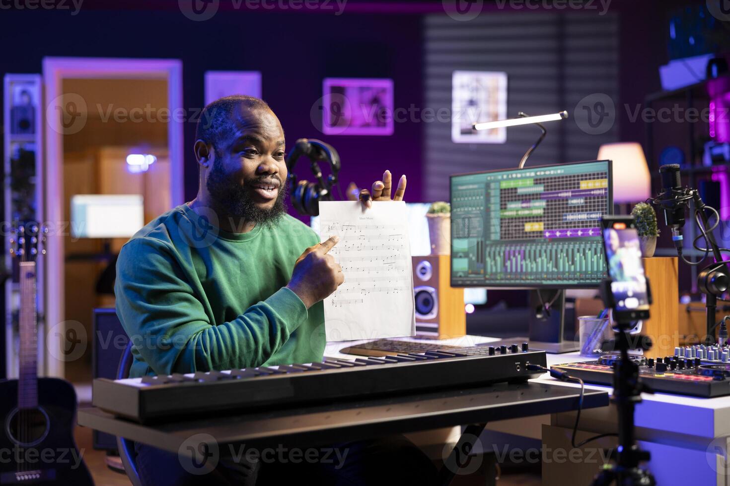 Young songwriter explaining music sheet with notes on online master class vlog, hosting internet lessons in his home studio. Artist composer teaching people how to sing on midi controller instrument. photo