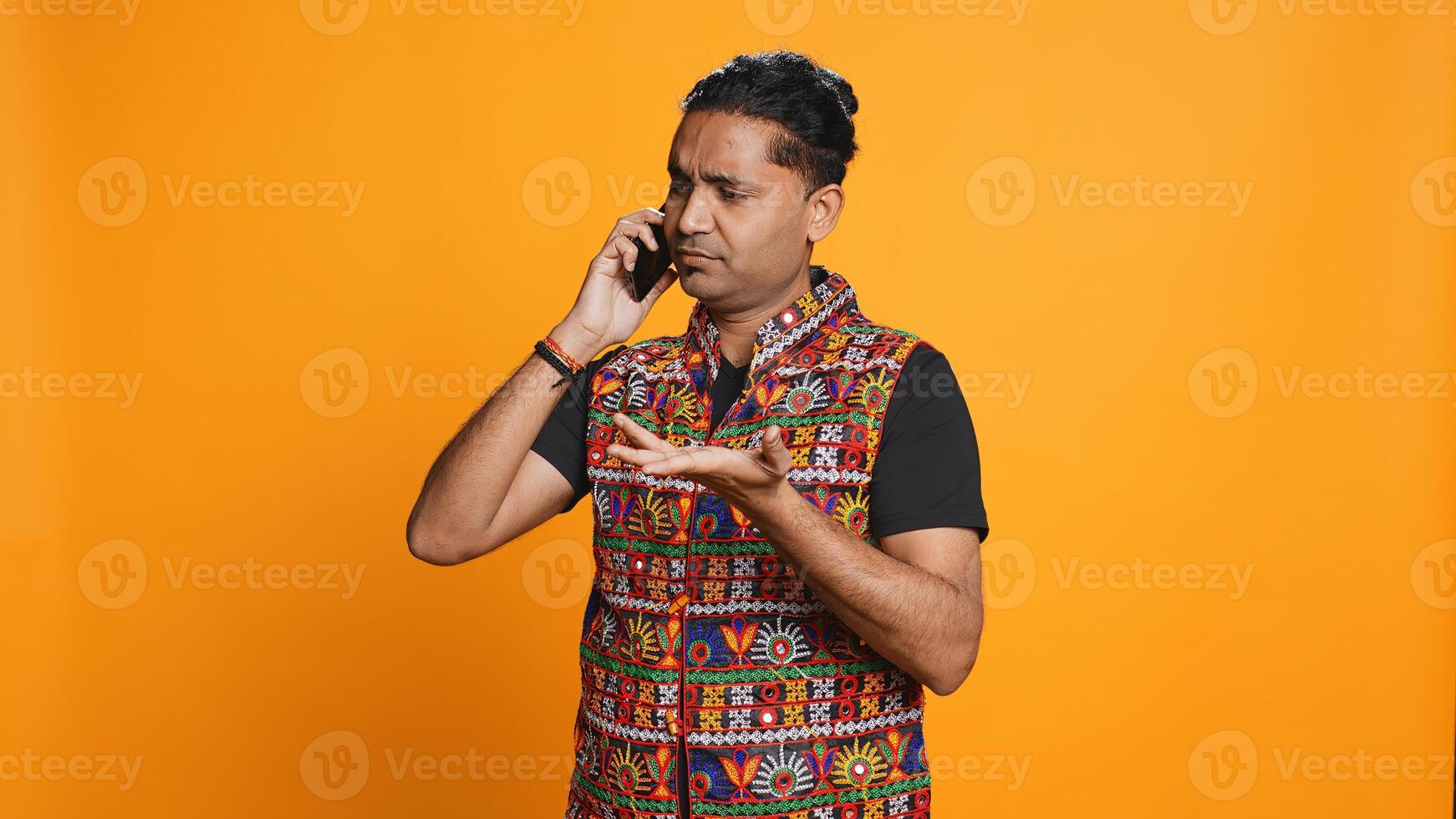 Indian man discussing with best friend over telephone call using smartphone. Cheerful person talking with mate in phone call using cellphone, isolated over studio background, camera B photo