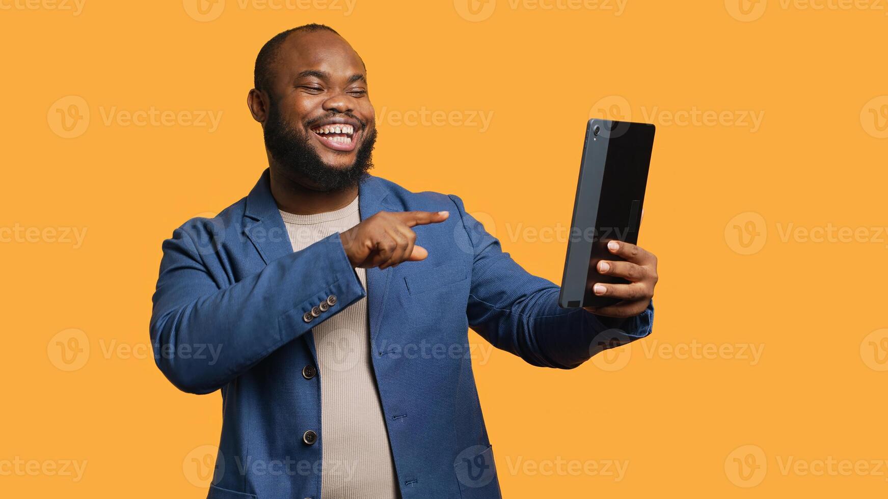 African american man having funny conversation with friends during teleconference meeting using tablet, studio background. Person laughing, having fun with mates during internet videocall, camera A photo