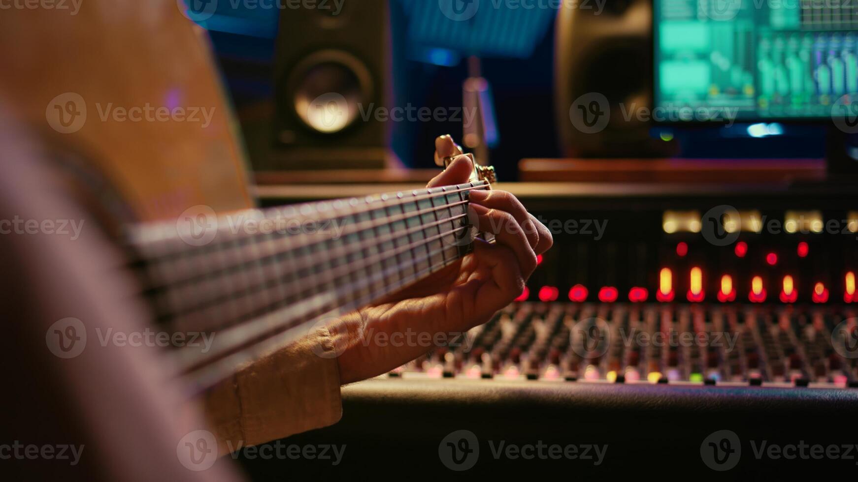 Skilled artist singing on his guitar and recording tunes for a future song, working on new album in control room at studio. Musician composer creating a new track on instrument. Camera B. photo