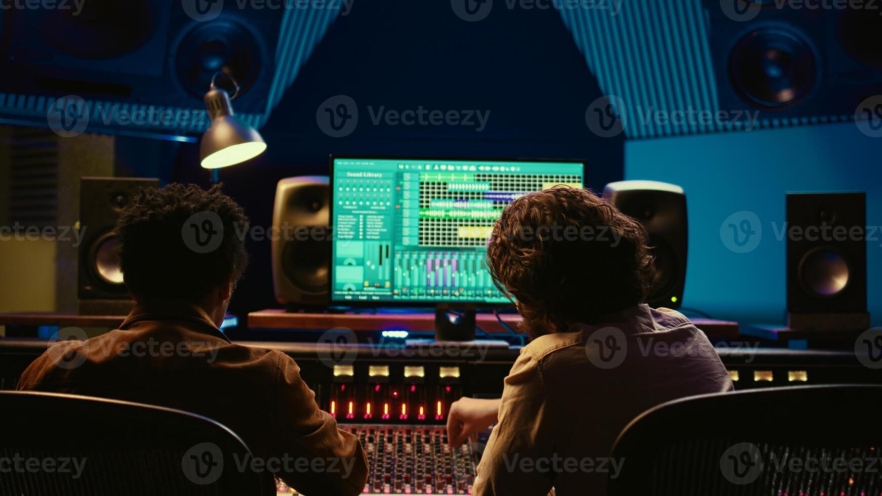 Sound designer working with artist to create a new song for his album, recording multiple tracks and editing them on audio digital software in control room. Producing new music. Camera B. photo