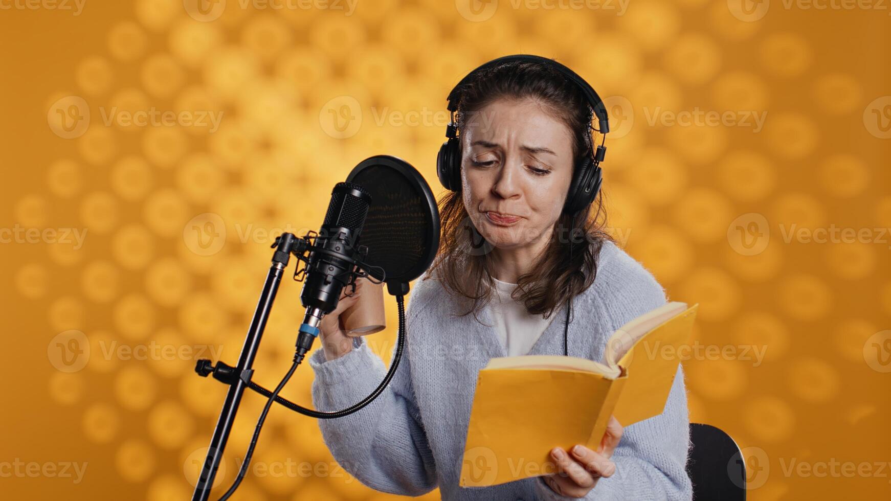 Voice actor reads book while enjoying coffee, recording audiobook using microphone, studio background. Woman using mic and headphones to produce digital recording of novel, drinking beverage, camera B photo