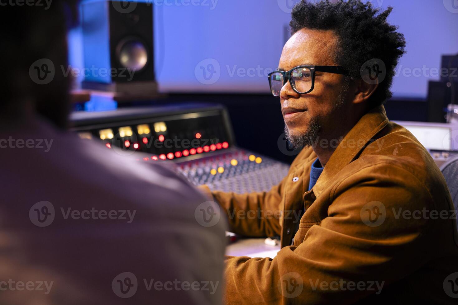 Audio technician and artist collaborating on music for pop rock album, processing and editing sounds with mixing console and software on computer. Singer works with producer for cool tracks. photo