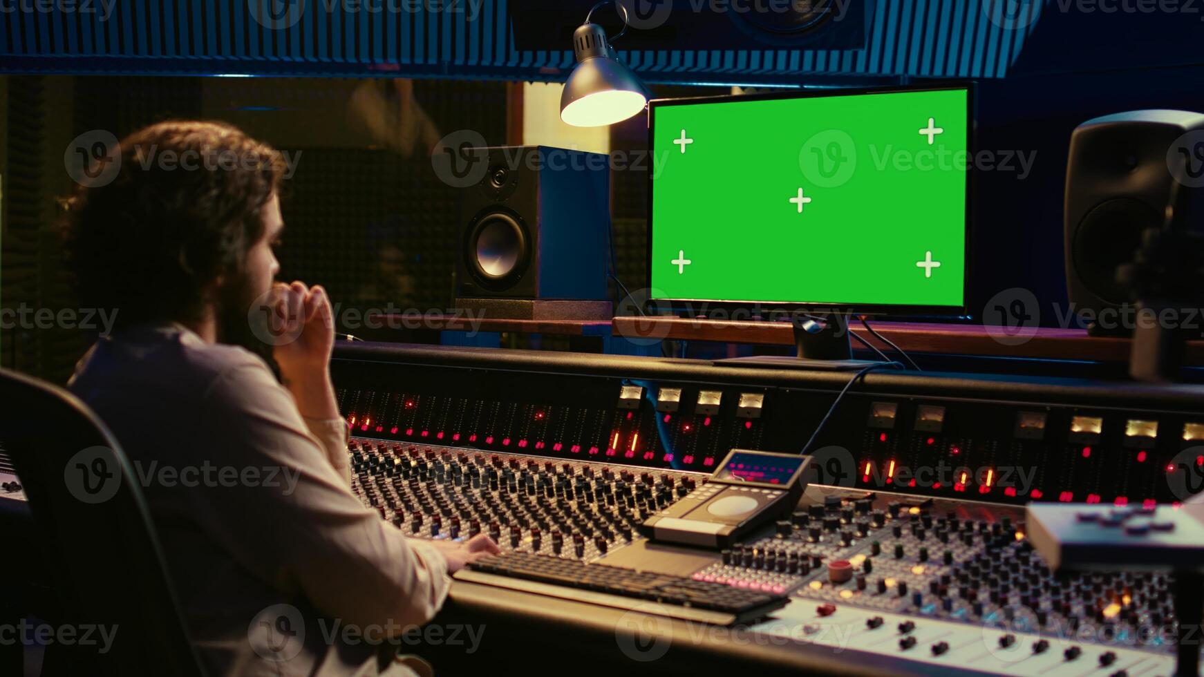 Sound designer watches online tutorials via greenscreen monitor to mix and master tracks and create music for his album. Audio engineer producing songs by twisting knobs and pushing faders. Camera B. photo