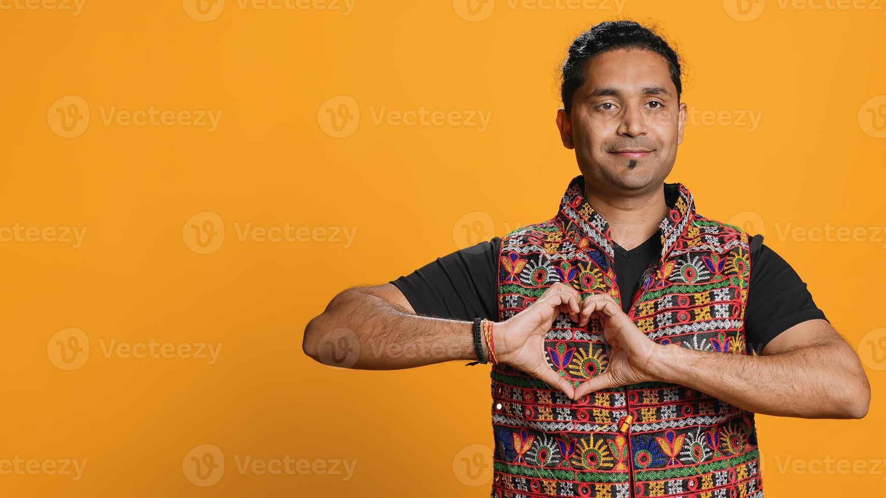 Portrait of jolly friendly indian man doing heart symbol shape gesture with hands. Cheerful nurturing person showing love gesturing, isolated over studio background, camera A photo