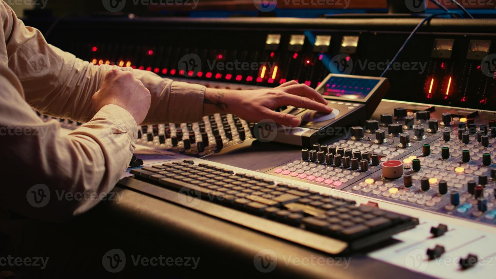 Audio technician uses mixing console and faders in control room, remote control for adjusting sound on mixer. Music producer changes volume level, creates tracks with technical equipment. Camera B. photo