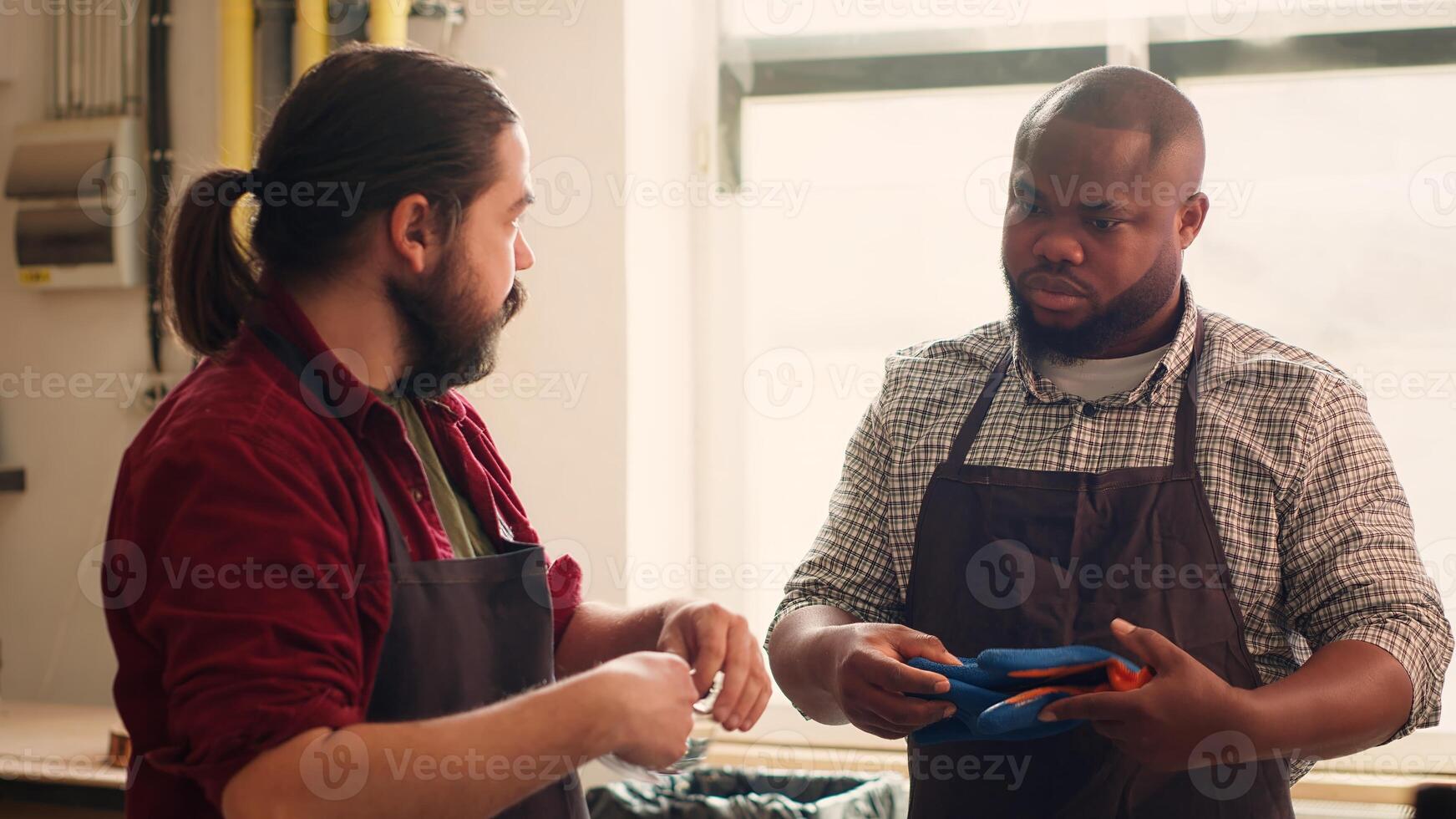 Master in woodworking shop giving BIPOC worker protection gloves before assembling furniture. Cabinetmaker preparing safety equipment for african american apprentice before starting work, camera A photo