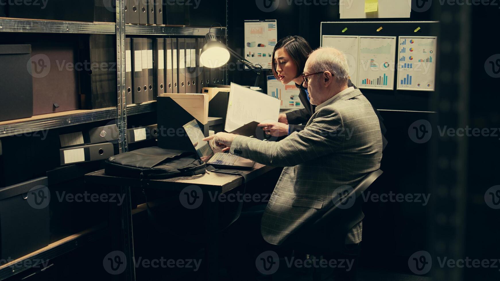 Detective team examines archived files for crucial case evidence, working in incident room with classified documents. Inspectors remain relentless in the pursuit of justice, police archive. Camera B. photo