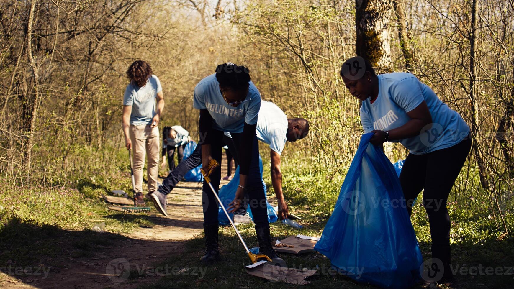 Environmental activists collecting rubbish and plastic waste in garbage bag, using littler cleanup tools to pick up trash from the forest. Women doing voluntary work to protect ecosystem. Camera B. photo