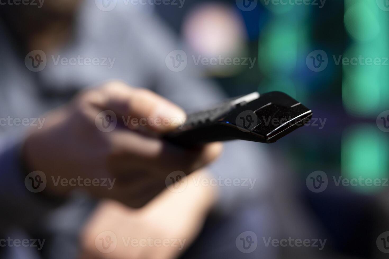 Focus on pointer device used by man in blurry background to zap through channels, resting in living room. Close up shot on remote control used by viewer to select TV station on television set photo