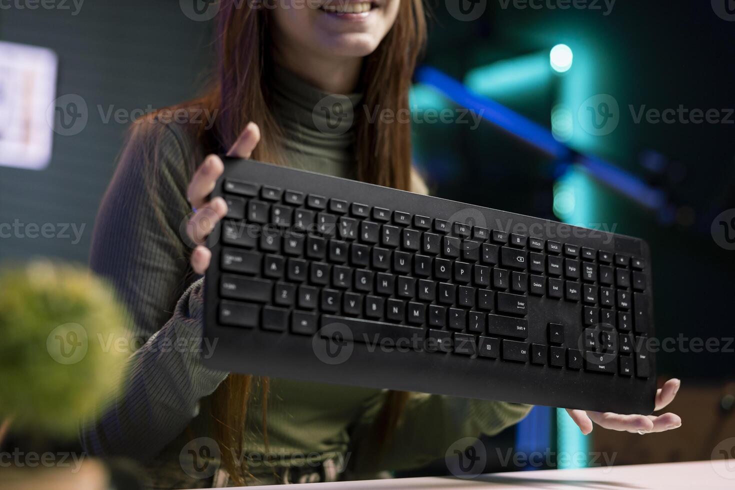 Woman presenting keyboard from brand sponsoring , advising fans to purchase it. Young online star does influencer marketing by advertising computer peripheral to fans, close up shot photo