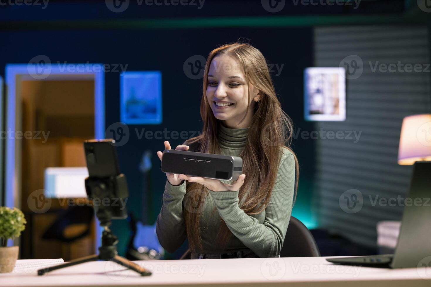 Happy teenage online star in apartment studio filming about best bluetooth music playing devices of the year. Upbeat young tech guru evaluating sound quality output of portable speaker photo