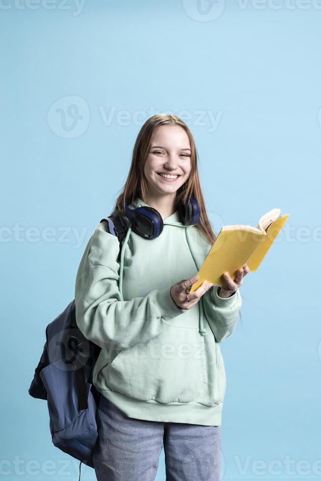 Portrait of happy young girl smiling while reading book, enjoying hobby, being entertained, studio background. Overjoyed woman entertained by novel, relaxing, having fun with interesting story photo