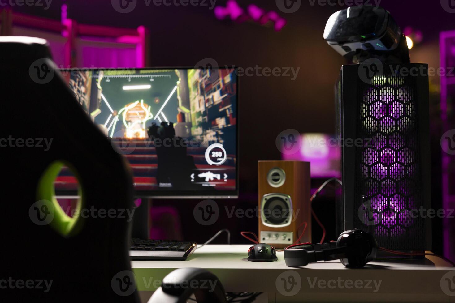 Empty neon lit living room with RGB lit computer on table next to headphones and high tech VR headset. FPS videogame left open on desktop pc display and virtual reality glasses in apartment photo