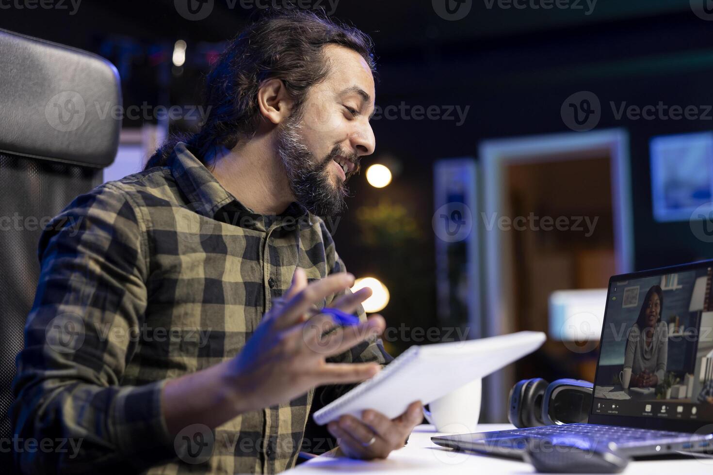 Closeup of young male university student communicating with his classmates on call, comparing notes through laptop. Smiling man grasping notebook while having a virtual meeting. photo