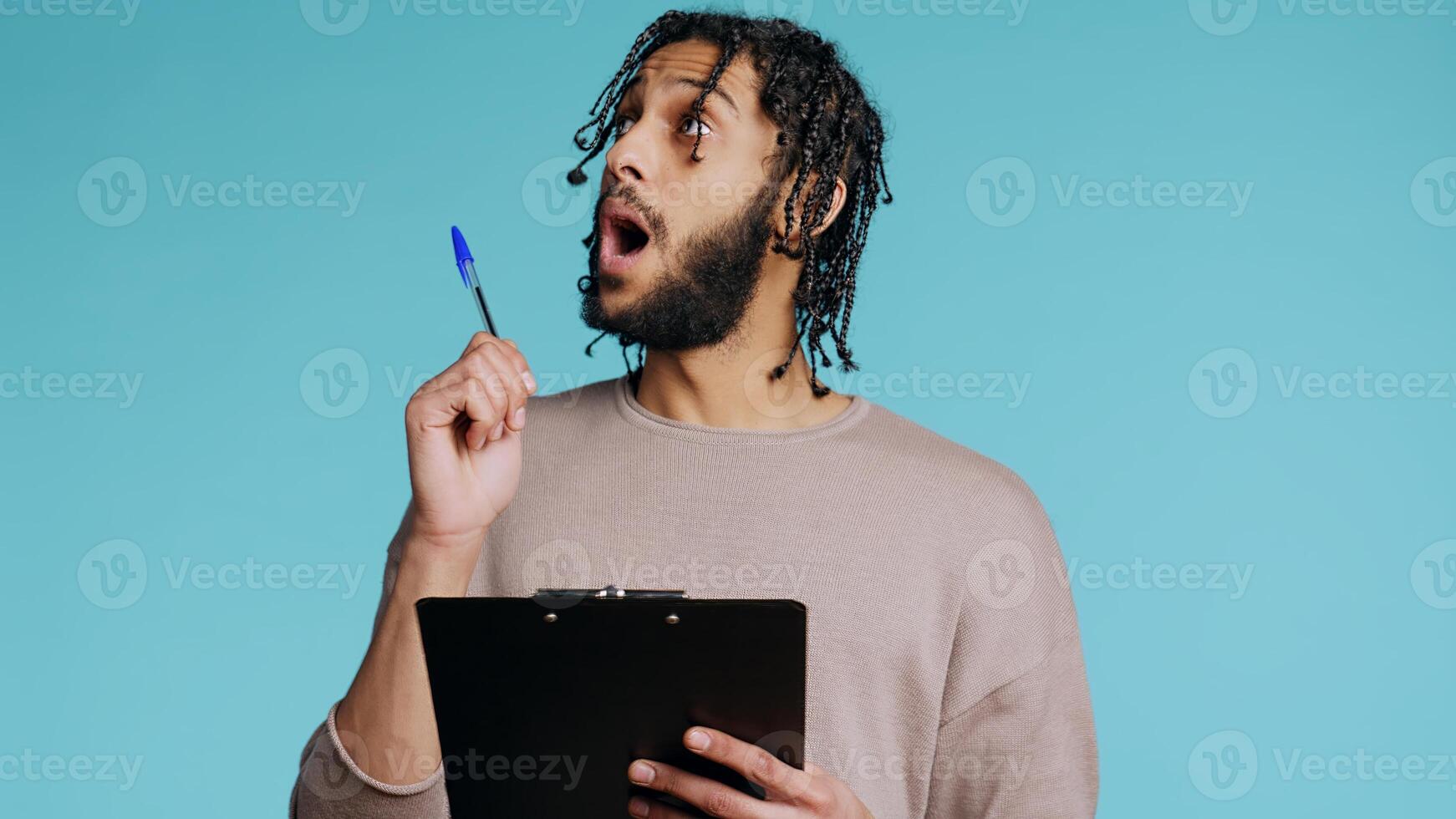 Creative man brainstorming ideas, writing on document using pen. BIPOC photographer using clipboard to complete shoot list for upcoming photography work, isolated over studio background, camera B photo