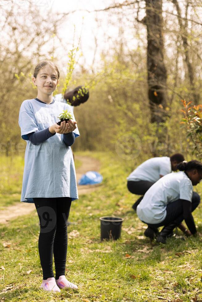 Small kid holding soil with green vegetation in her hands, contributing to environmental conservation and protecting the natural habitat. Young girl activist doing voluntary work to save the planet. photo