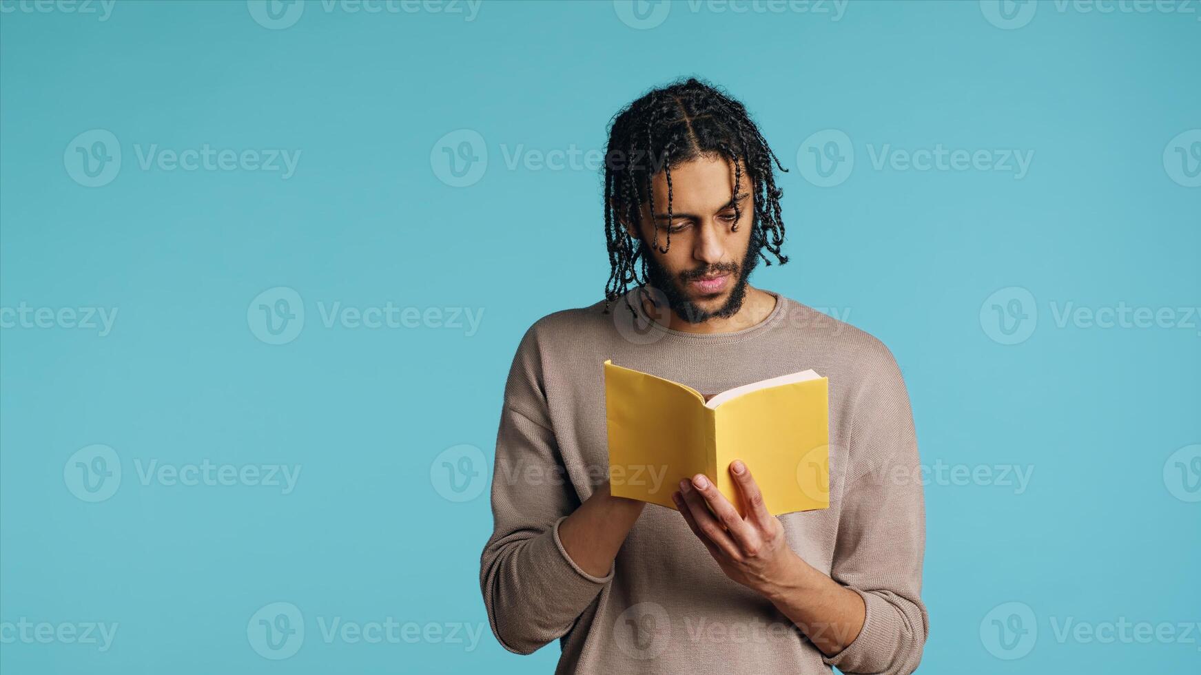 Middle Eastern man reading newly released hardcover book from publisher, entertained by engrossing story. BIPOC person enjoying literature novel during leisure time in studio background, camera A photo