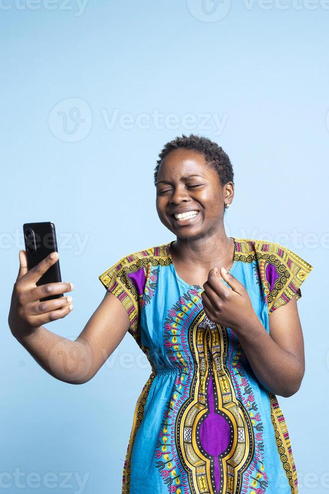 Young adult laughing at videocall online on smartphone, having fun chatting with her friends on teleconference web connection. African american girl enjoying internet discussion on videoconference. photo