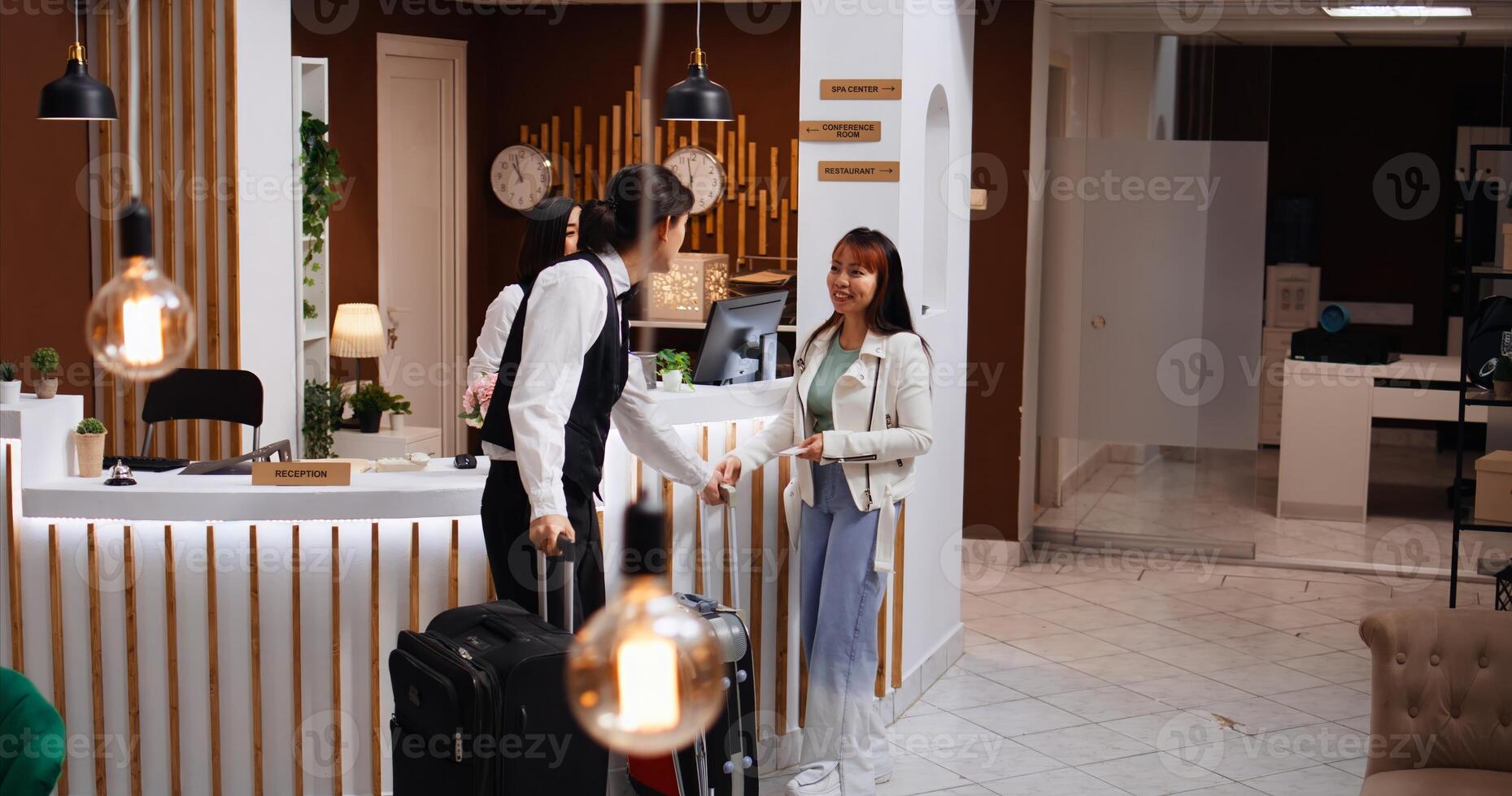 Receptionist finishing check in and giving back passport to client. After confirming room reservation and id, front desk staff provides room access key card for asian traveler, tourism concept. photo