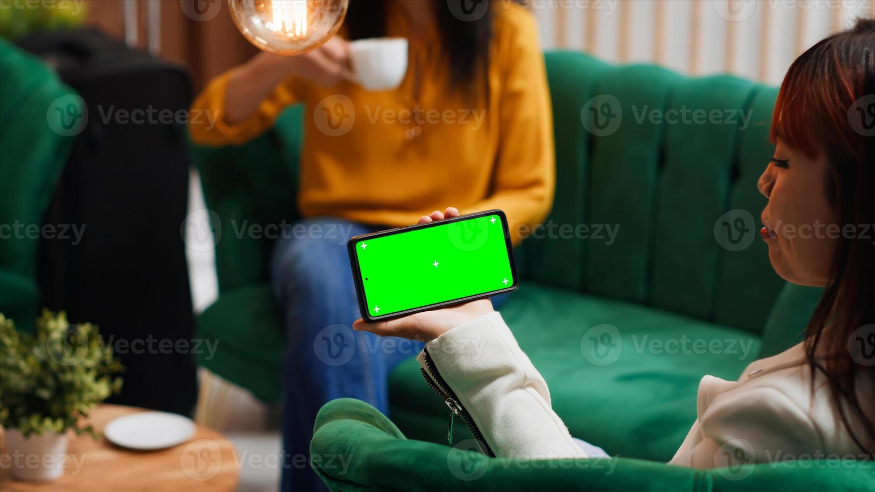 Asian woman holding phone with isolated greenscreen in lobby, looking at display with chromakey template and mockup copyspace layout. Traveler using device and relaxing at hotel. photo