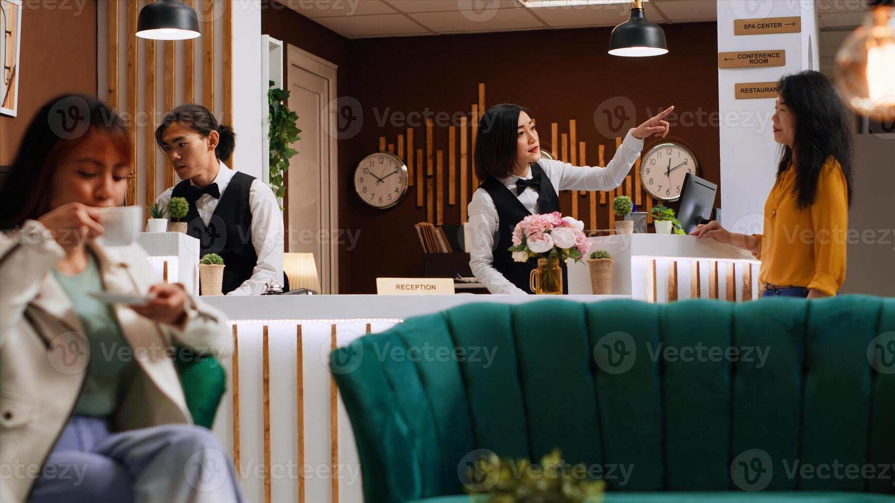 Hotel guest asking staff about amenities at holiday retreat, talking to front desk worker about reservation and check in. Asian receptionist greeting customer in lobby. Handheld shot. photo