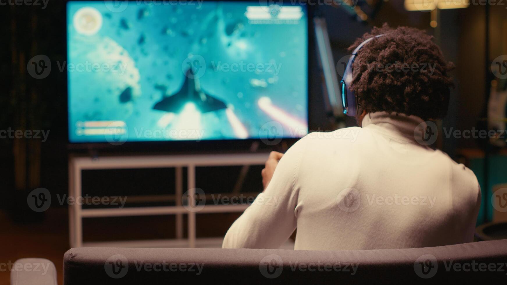 Gamer putting on headphones to feel immersed in intense classic arcade space shooter videogame. Man relaxing in apartment using high tech gaming system to play singleplayer game photo