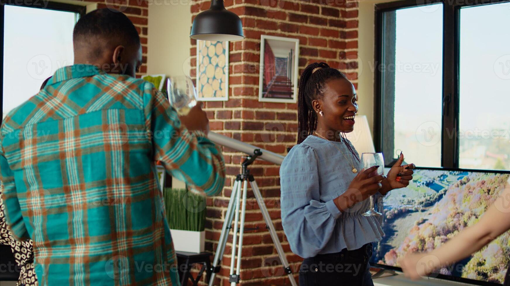 BIPOC group of friends dancing at apartment party, having fun together , holding wine glasses. Multiethnic people doing energetic dance moves on vibrant music in brick wall living room photo