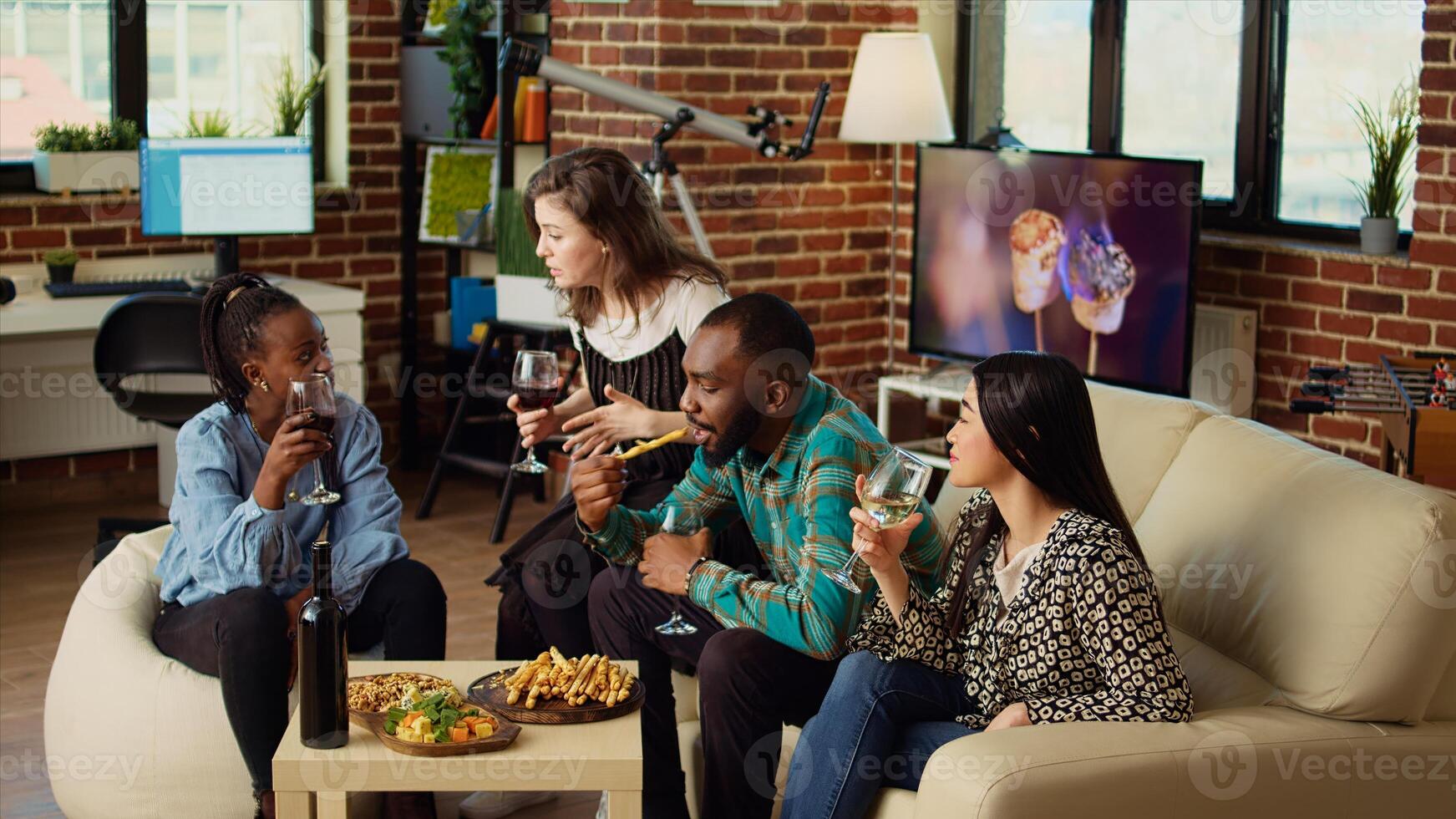 Woman having interesting conversation with BIPOC apartment party guests, sharing engaging story with them. Host chatting with happy multiracial friends in brick wall living room photo