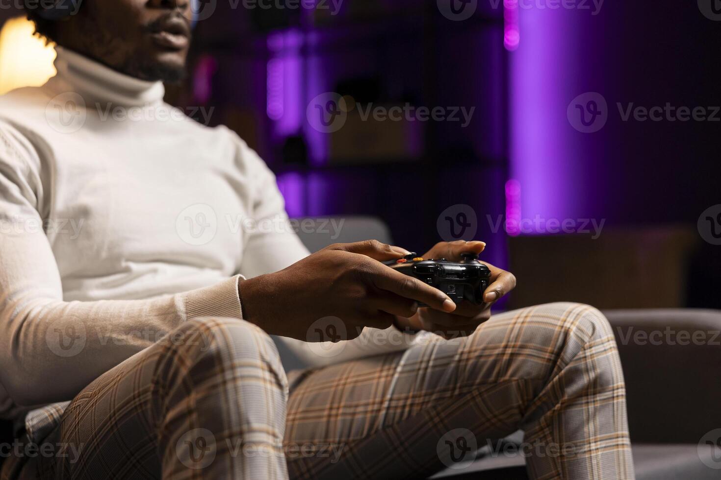BIPOC man playing intense online videogame in neon illuminated living room, spamming buttons on controller. Gamer participating in internet esports competition, playing on gaming console, close up photo