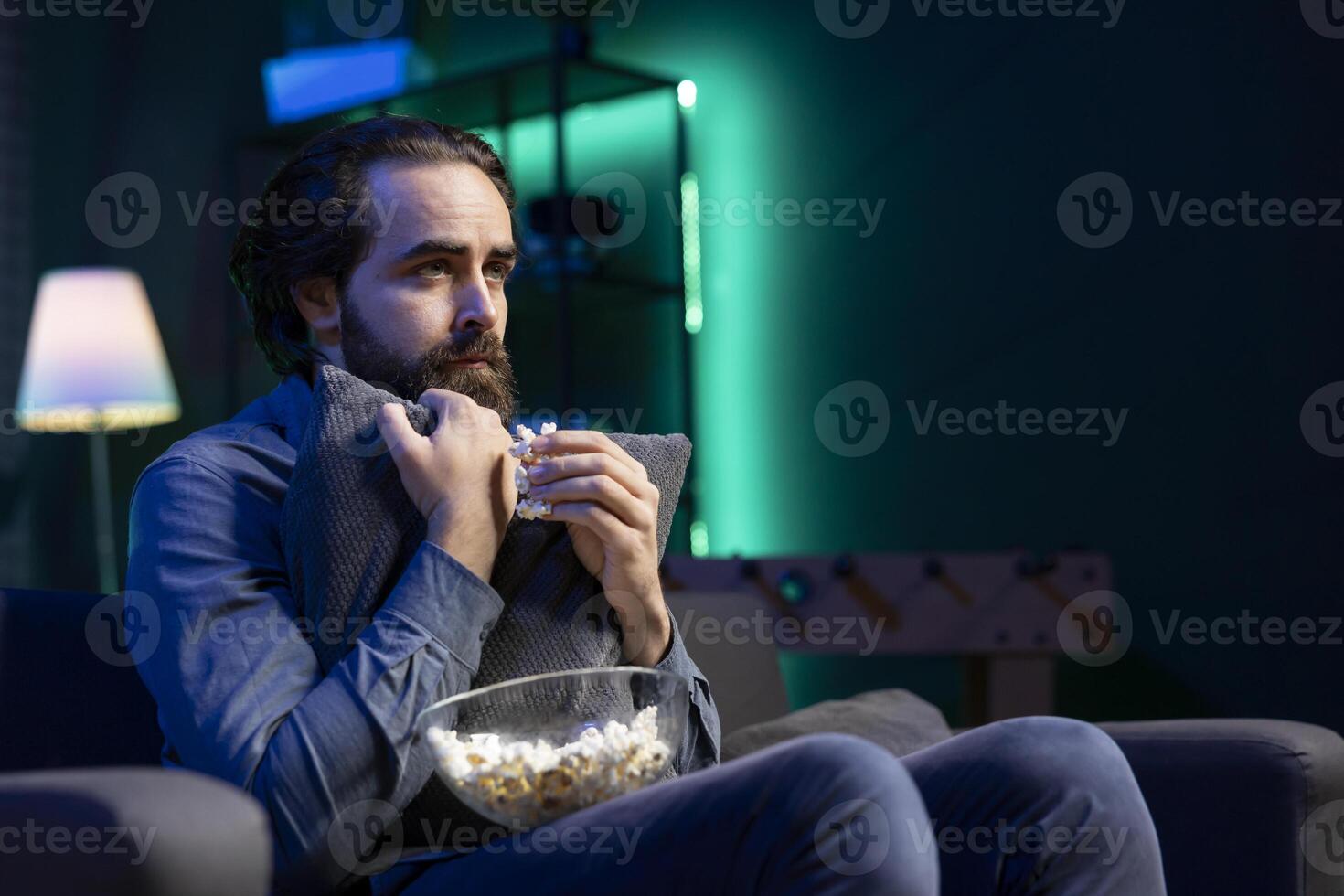 Sad man watching drama movie on online streaming service in apartment, enjoying time off from work. Person on couch hugging pillow, feeling affected by film broadcasted on TV photo