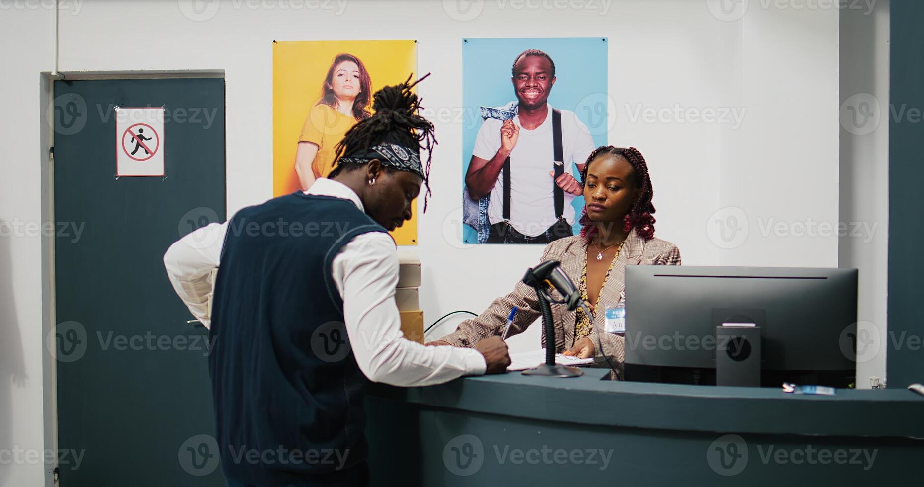 Retail employee picking up clothes order boxes from department store, signing invoice and confirmation papers at cash register counter. African american woman giving requested merchandise. Camera B. photo
