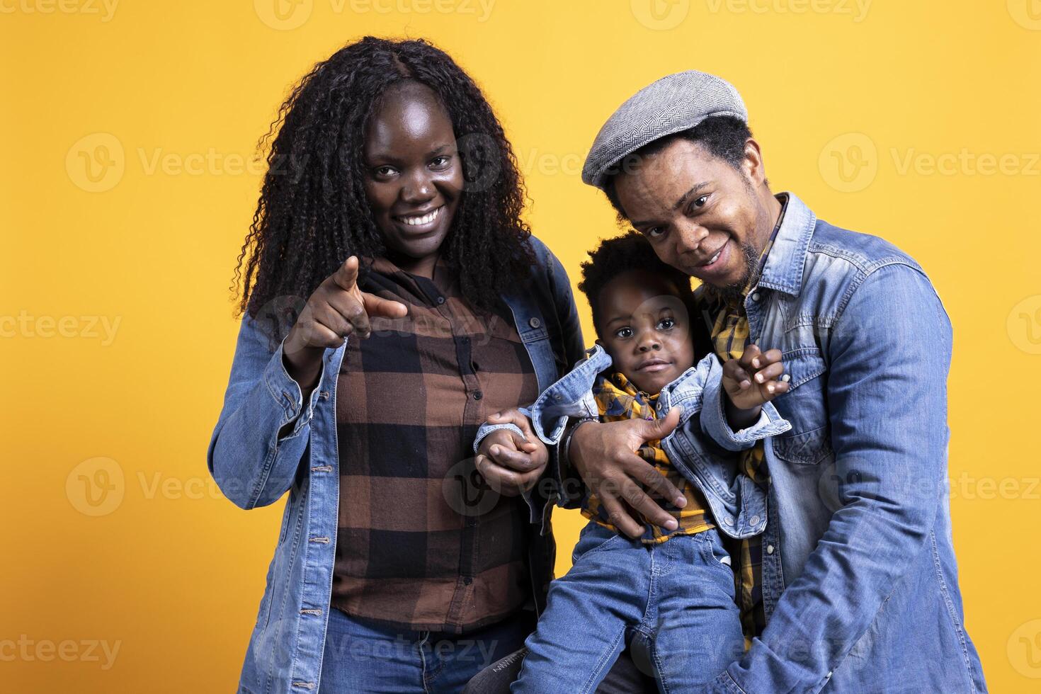 Smiling loving young family with a small cute toddler posing on camera, mom and dad hugging their child against yellow background. Happy peaceful couple with a little baby boy. photo