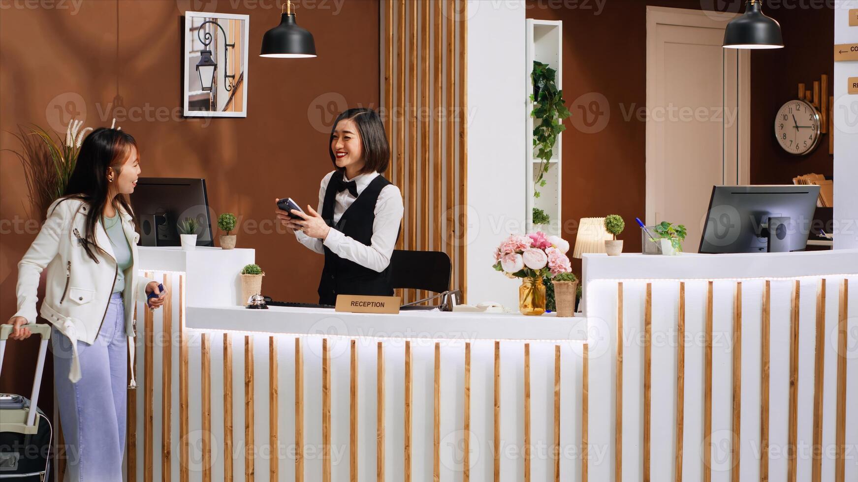 Asian traveler paying for hotel room during check in process, choosing pos terminal payment with credit card. Young woman with luggage making electronic transaction for accommodation. photo