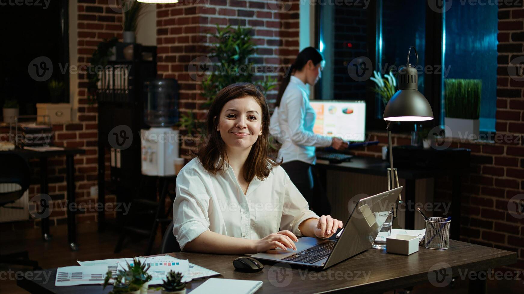Portrait of smiling businesswoman planning marketing project on laptop late at night. Cheerful office worker working nightshift, making strategy research to create financial development, camera A photo