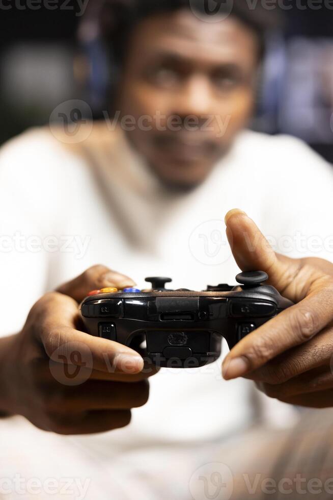 Focus shot on controller held by man defeating enemies while playing videogames on gaming console with teammates. Player in blurry background using gamepad to participate in esports game photo