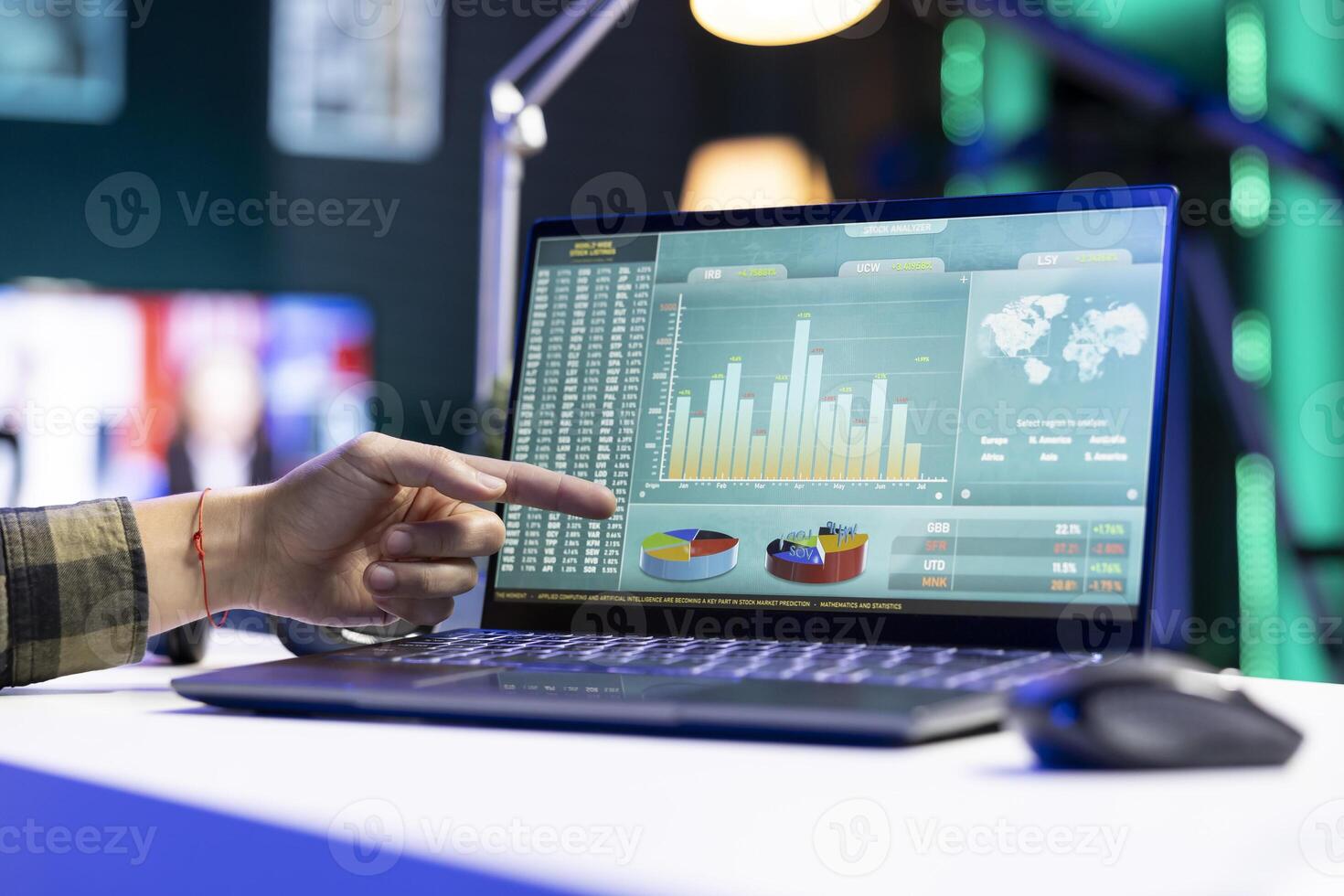 Closeup of a person pointing towards screen displaying financial charts and numbers, representing stock trading. Digital laptop on a desk showing forex trend values and graphs. photo