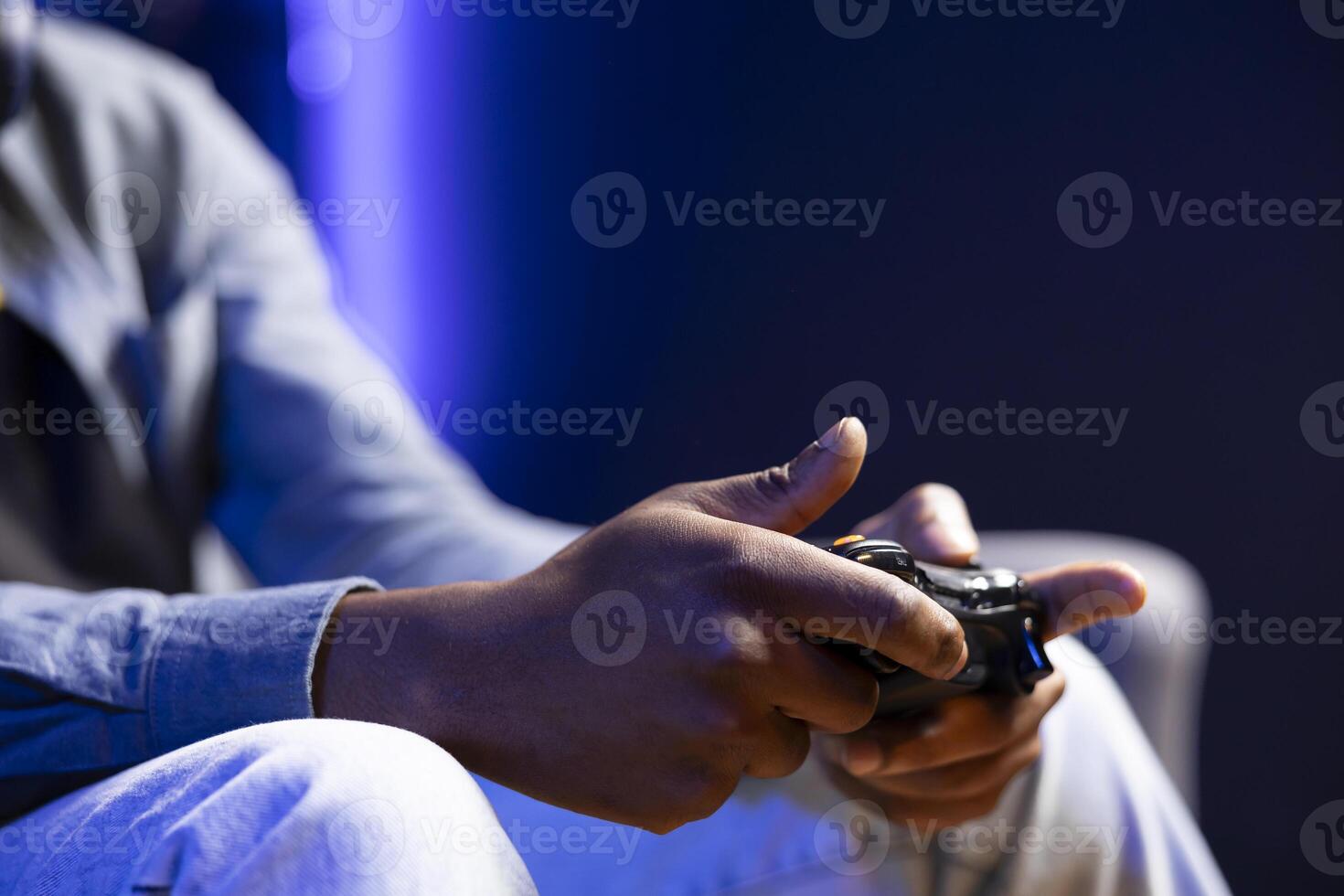 Gamer in RGB lit home gaming with gamepad, enjoying himself. Close up shot of man sitting on sofa in neon illuminated living room, playing videogames on console using controller photo
